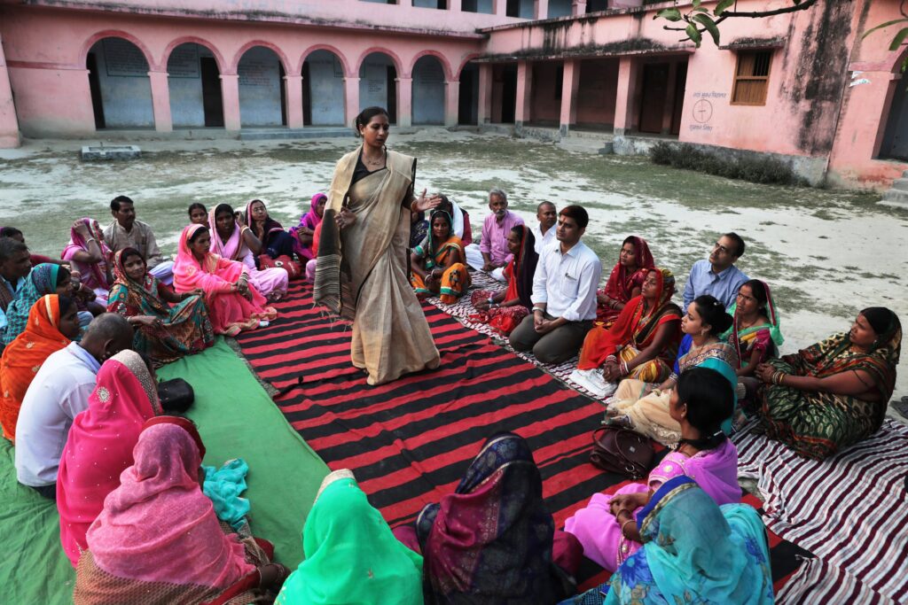 Woman speaks to a group of people sitting around them in a circle.