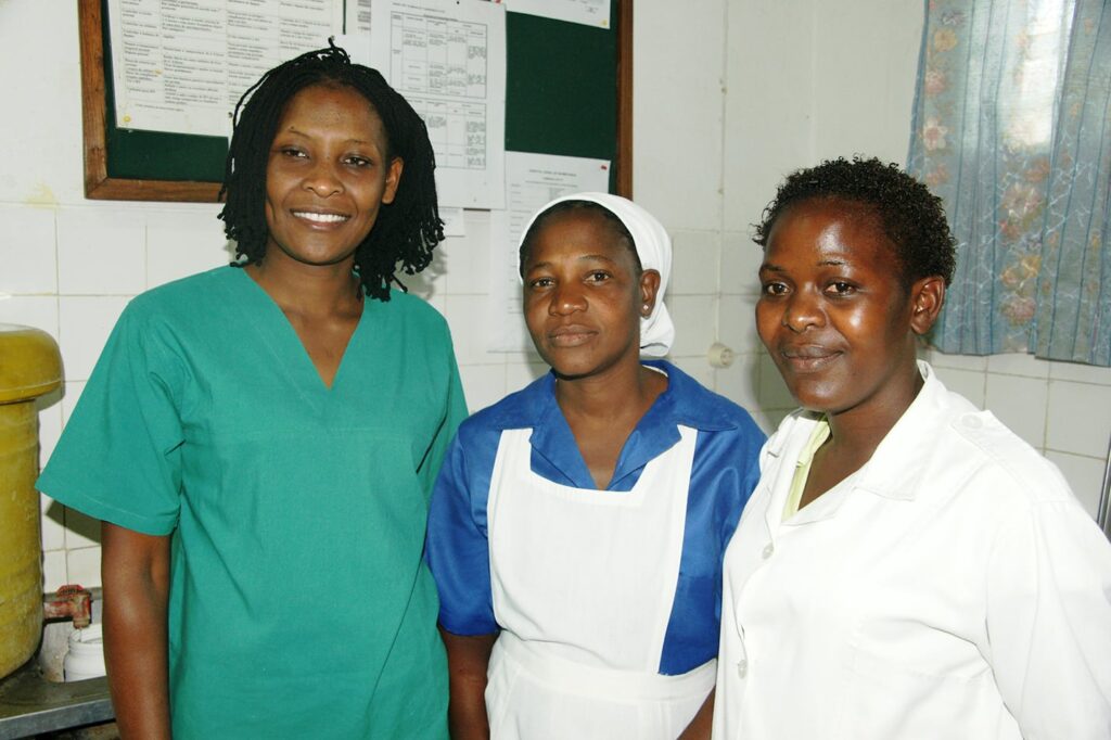 Three healthcare providers smile at the camera in front of a bulletin board in a room.